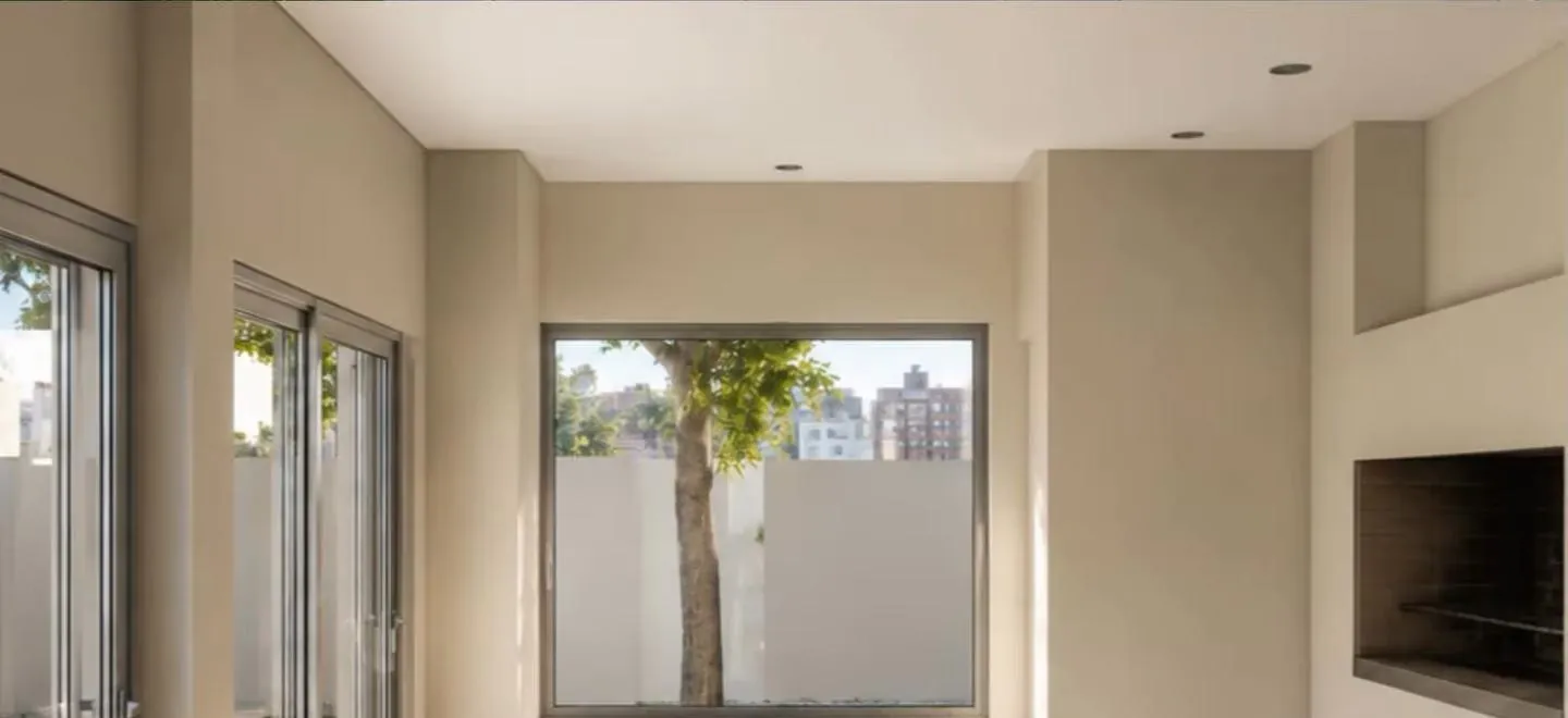 Interior del quincho con aberturas al patio, ventana hacia el árbol y parrilla